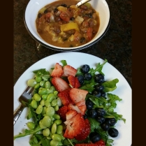 Arugula dressed in olive oil, lemon juice and balsamic topped with fresh strawberries, blueberries, and blend of edamame and limabeans with a bowl of vegan chili