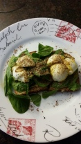 Spinach, flaxseed, and a soft boiled egg on top of a slice of toasted multigrain bread with jalapeño and garlic hummus spread.