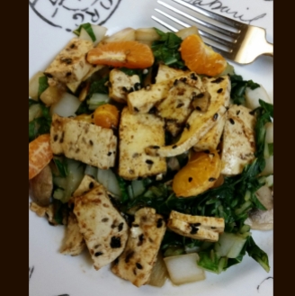Sauteed tofu atop bok choy, sprinkled with black sesame seeds and clementines.