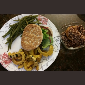 Veggie burger and lettuce between Sandwich Skinnys Bread with a side of green beans and baked delicata squash. Alongside, a bowl with cinnamon baked pear topped with a wild rice blend.